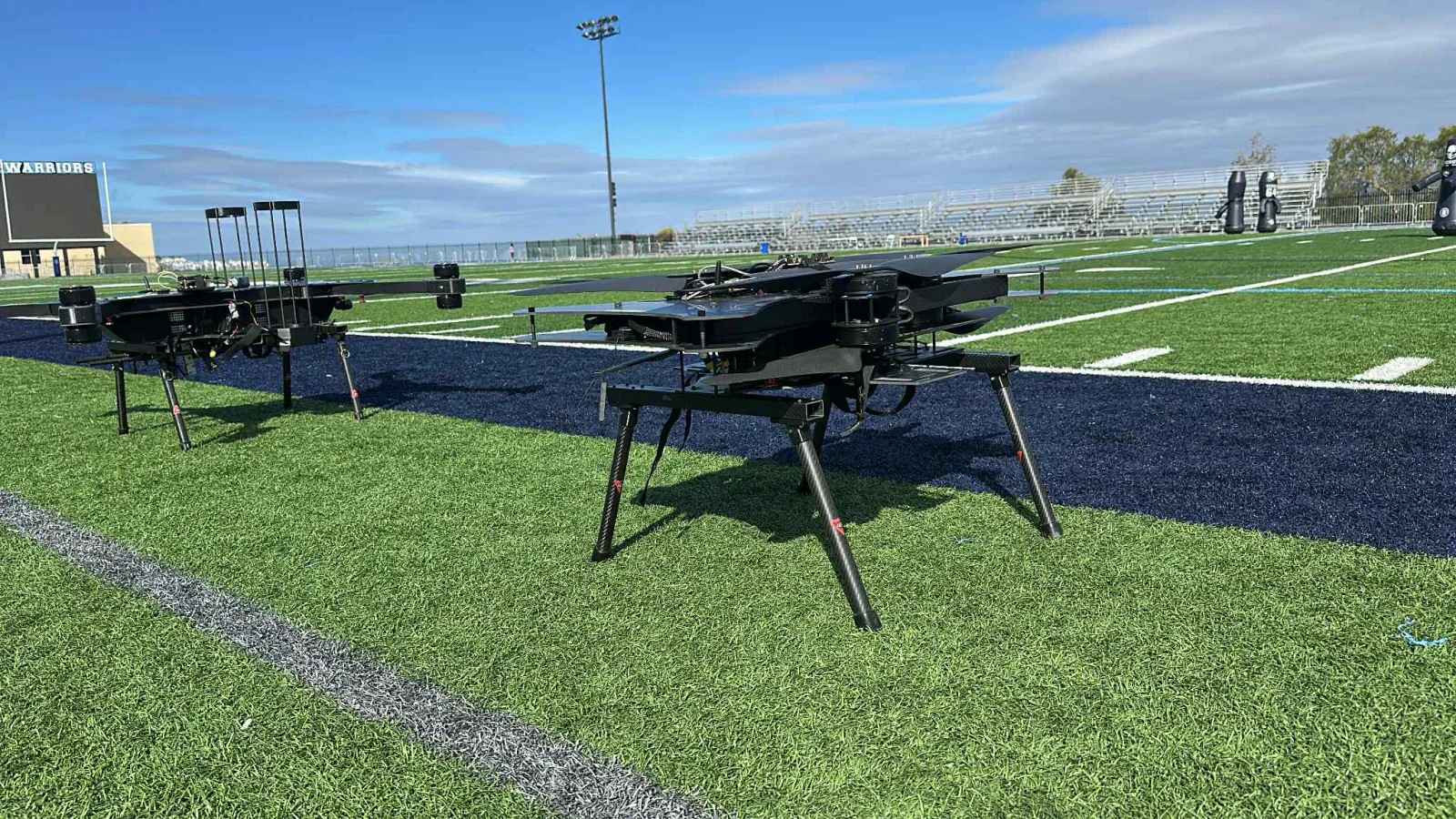 Two large black multirotor aircraft parked on a sports field under a clear sky