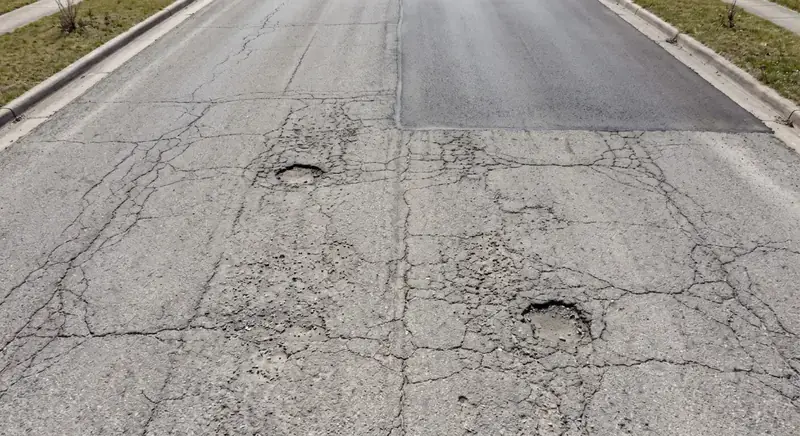 حارة إسفلتية متشققة فيها حفرتان مفتوحتان
