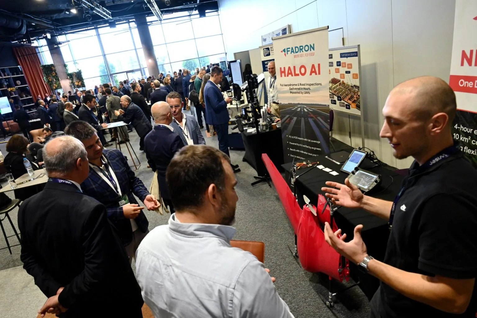Besucher im Gespräch mit einem Fadron-Ingenieur neben einer roten Nimbus auf dem Fadron-Stand auf einer belebten Industriemesse