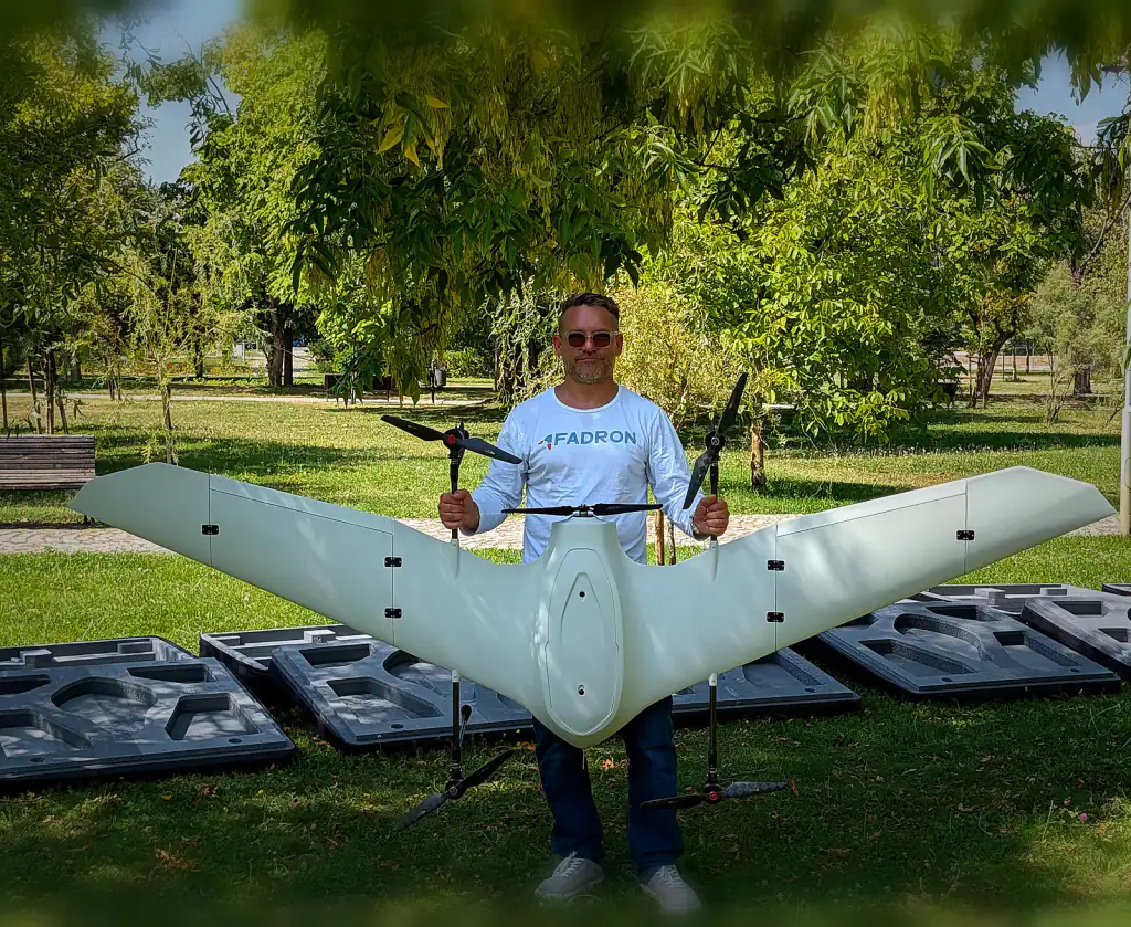 Fadron engineer holding a white Nimbus VTOL drone with its lift rotors fitted, standing on grass in a park
