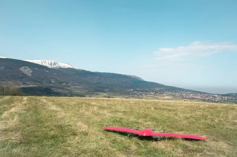 Red Nimbus VTOL drone on a grassy upland field ready for vertical take-off, with snow-capped mountains behind