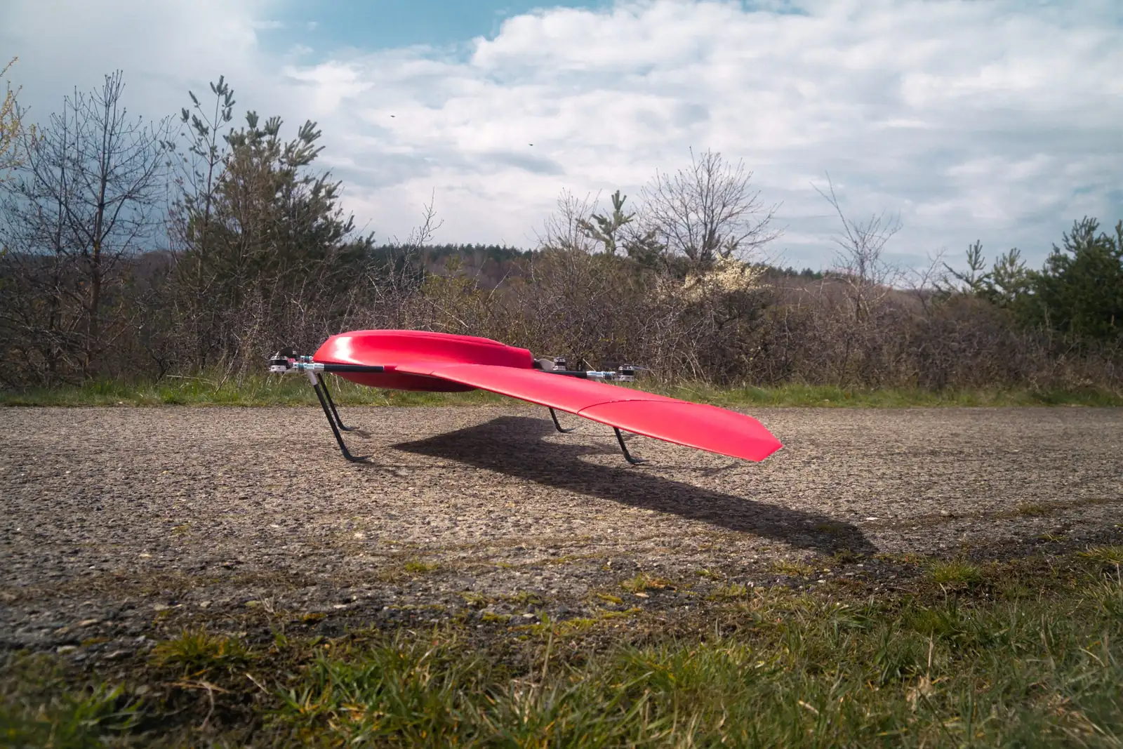 Nimbus VTOL standing on its landing legs on a gravel strip, scrub and trees behind under a cloudy sky
