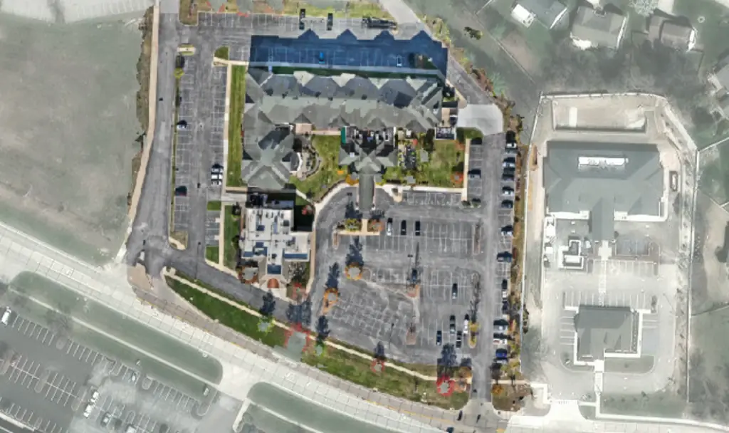Drone image of a parking lot beside an apartment complex, with parked cars, stall lines and landscaped islands, before HALO AI analysis