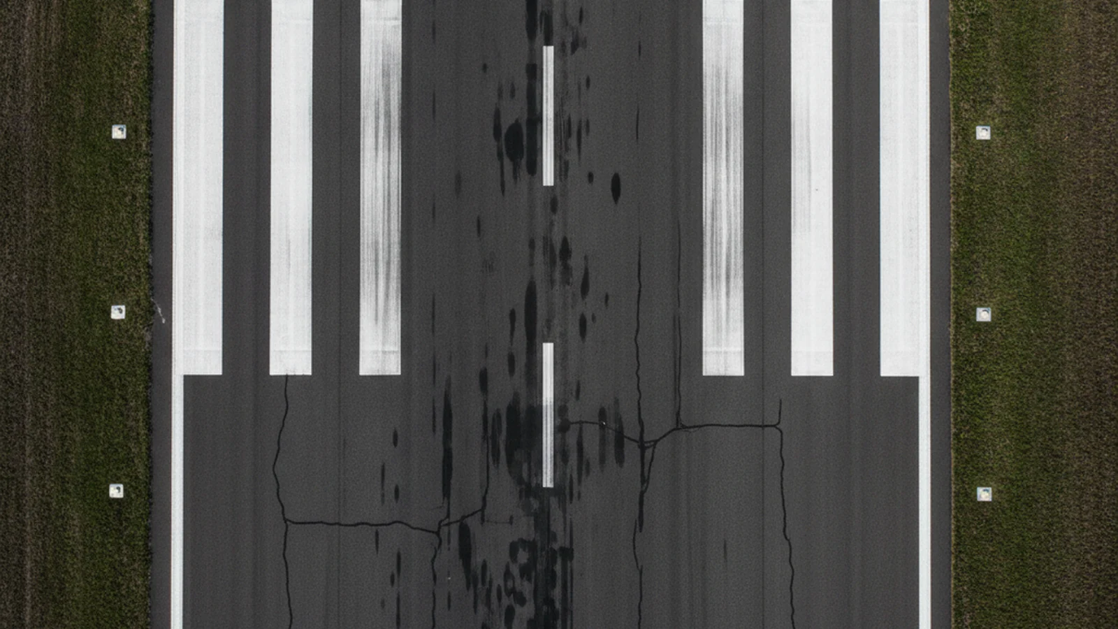 Runway threshold seen from directly overhead, threshold bars and centreline across weathered asphalt