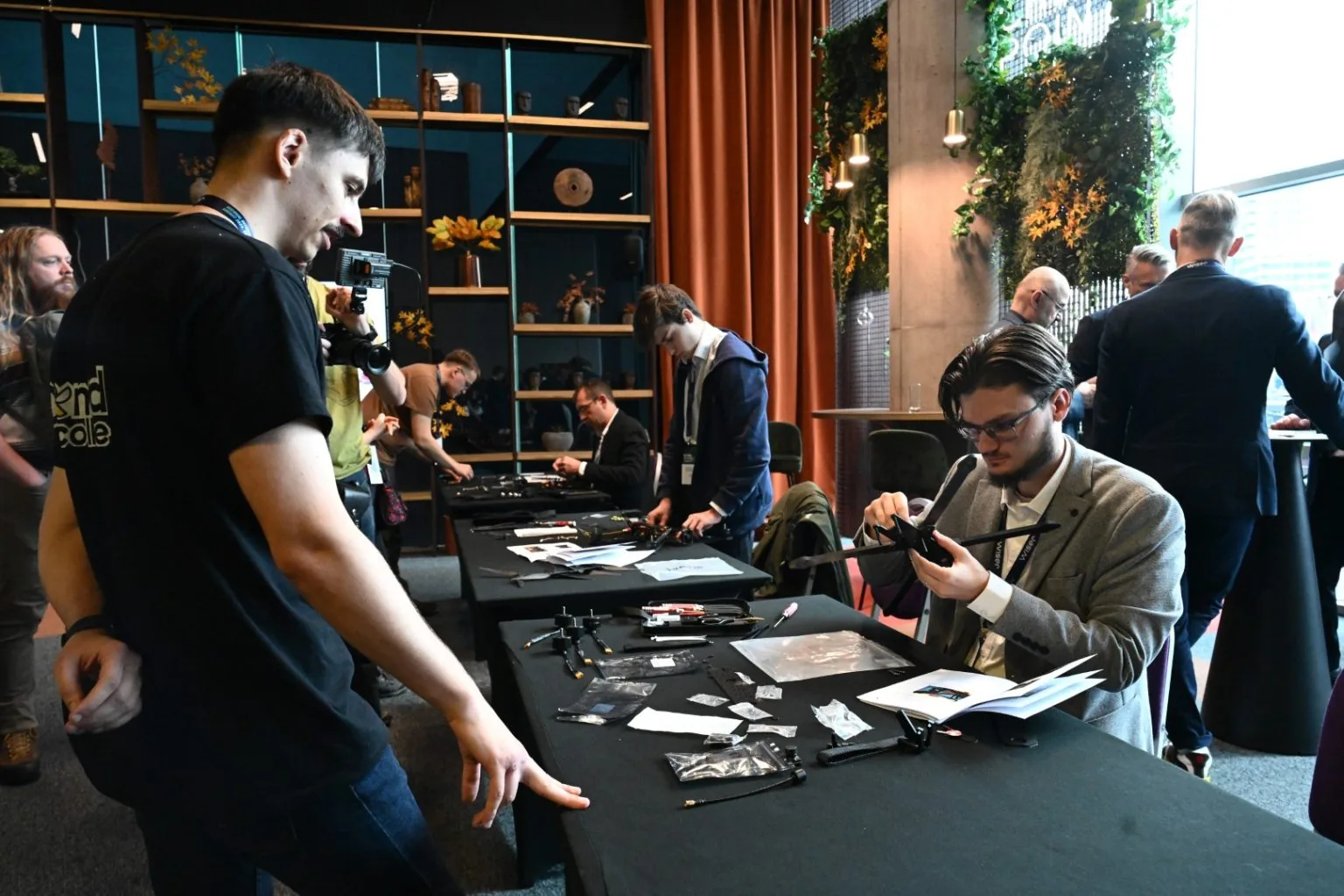 Drone components, tools and airframe arms laid out across workbenches at a build session